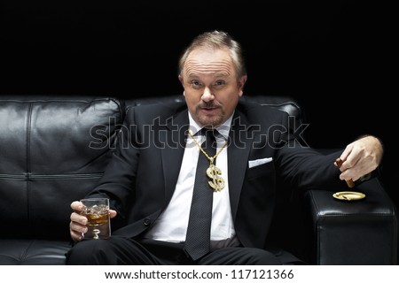 Handsome mafia boss drinking and smoking while sitting on a couch