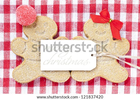 Close-up top view of gingerbread couple with merry Christmas tag over red checked napkin.