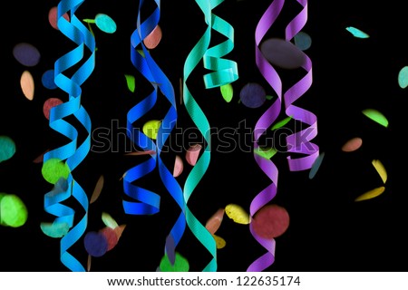 Detailed cropped shot of colorful decorative streamers and confetti over plain black background.