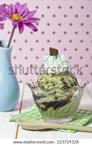 Close-up image of mint ice cream with melted chocolate syrup and a flower vase on the side