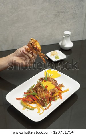 Cropped image of a human hand holding a crab while eating crab dish.
