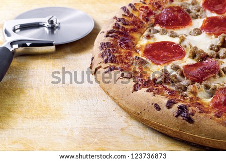 Freshly baked pepperoni and cheese pizza with pizza cutter on wooden board