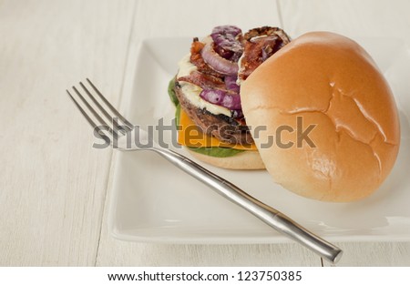Close-up image of a plate of burger sandwich with a fork on the side