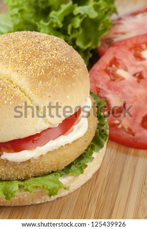 Closed up shot of yummy chicken burger laid in a wooden table topped with tomato slices and lettuce leaves