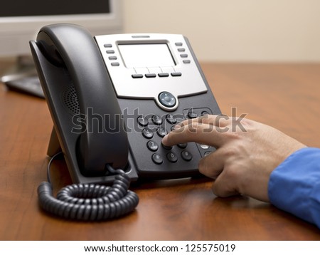Detailed shot of a human hand dialing number on landline phone on office desk.