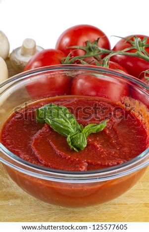 Bowl of tomato sauce with raw tomatoes and mushroom on wooden board