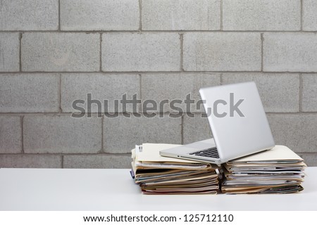 Laptop resting on 2 stacks of files with a brick background.