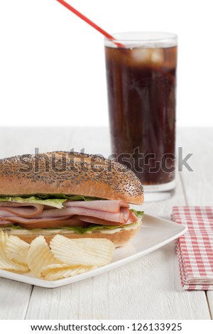 Close-up image of a ham sandwich with cola and potato chips on the wooden table