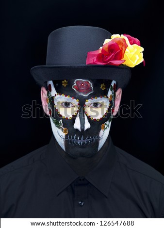 Portrait shot of a scary man wearing traditional sugar skull make-up and hat decorated with roses over plain black background.