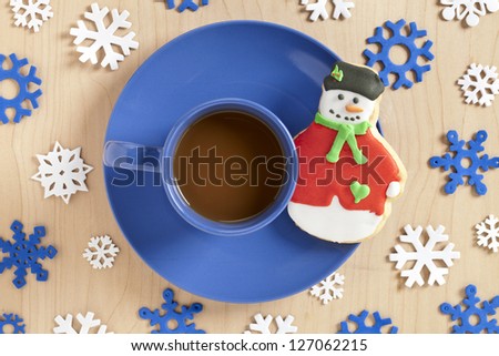 Close-up overhead shot of a coffee cup with snowman cookie on blue saucer with snowflake design on table.
