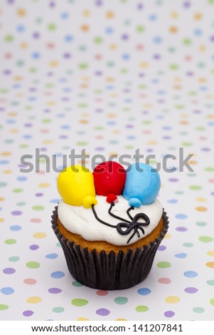 Close-up shot of cupcake with multi colored balloons  over polka dots background.