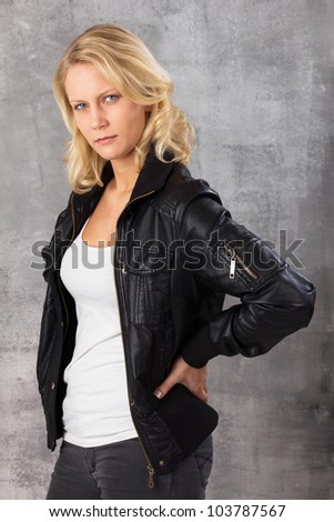 Portrait of a self-confident modern woman with hands on hips looking at the camera. Studio shot against a gray background.
