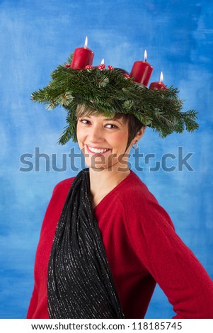 Beautiful smiling young woman woman wearing advent wreath on her head, four candles are burning. Studio shot with copy space against a blue background, series