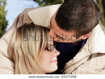 Couple in love, outdoor shot of two young people, the man kisses the woman on the forehead.