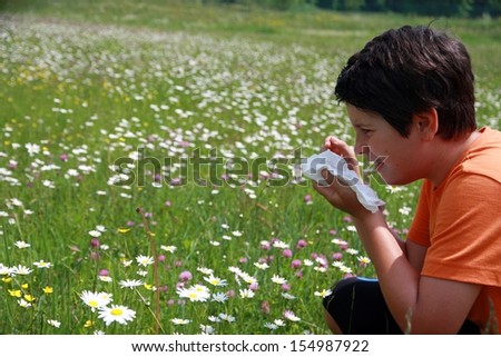 allergic child to pollen and flowers with a handkerchief while sneeze in the middle of meadow
