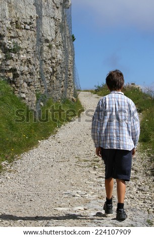 lonely child walks on the mountain path next to the huge wall of an ancient fortification of World War I built with stones