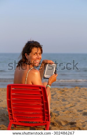 beautiful smiling woman reads the ebook on the beach by the sea