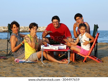 happy family of five person  eats pizza on the beach at sunset on the sea