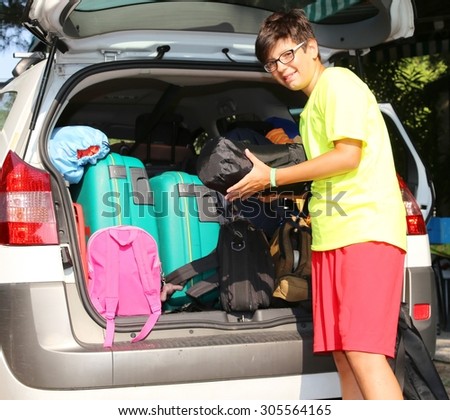 smiling boy loads bags in the baggage car in summer
