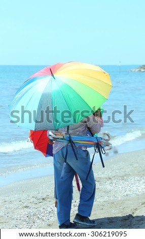 Elder peddler of colorful umbrellas by the sea on the beach in summer