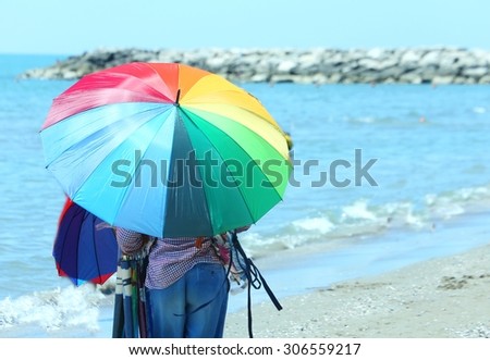 Elder peddler of colorful umbrellas on the beach in summer