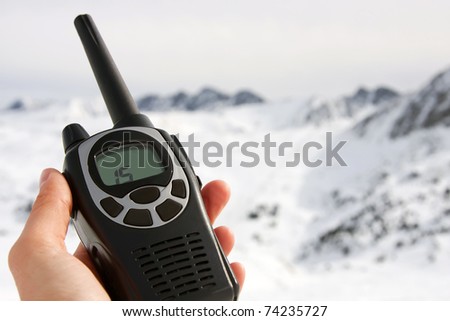 Black walkie talkie in a hand, mountains on the background