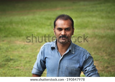 Portrait of a young Indian male with receding hair and serious look of a businessman or an entrepreneur with green background