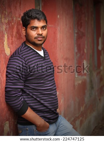 indian man leaning on a wall causally, relaxed, looking at camera. The person can also represent a latin or a mexican businessman