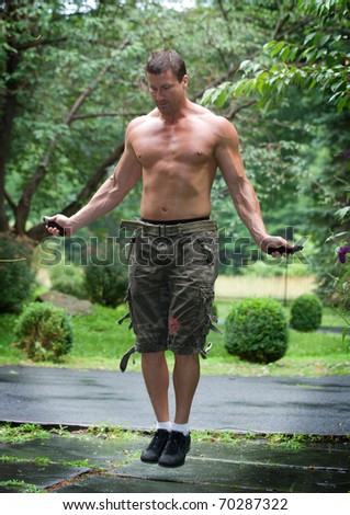 Man jump roping with shirt off in the outdoors.  Ripped muscles and six pack abs. Jumping at a high speed.