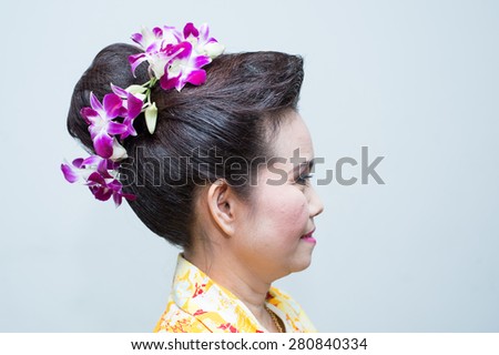 the right hand side of middle aged Thai woman with hair bun and orchid around