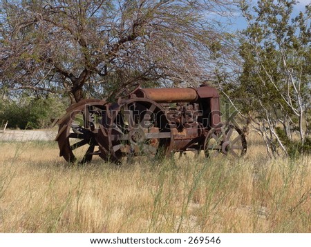 Rusty tractor in desert with metal wheels, side view.