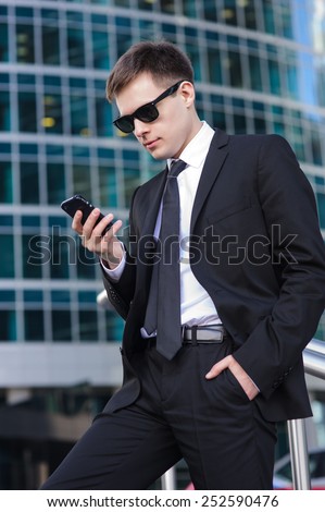 Businessman looking at his phone in his right hand and holding his left hand in his pocket.