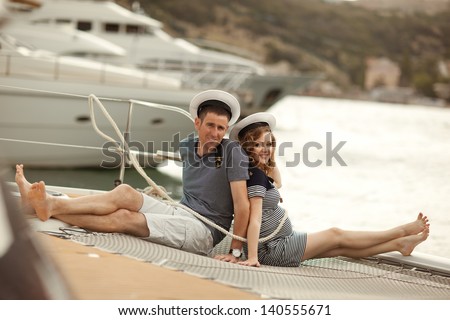 funny couple husband and pregnant wife are sitting back to back on a yacht at sea.