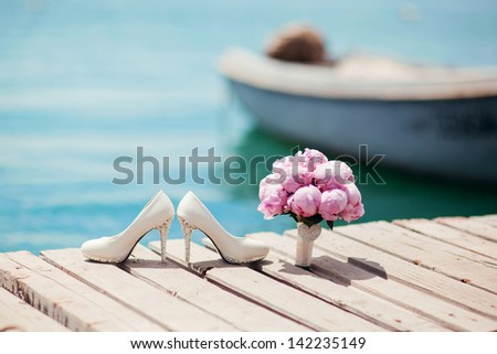 beautiful white wedding shoes and bouquet of flowers by the sea