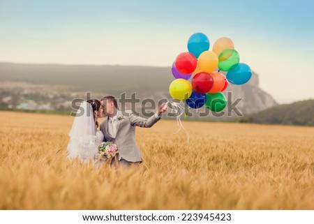 Wedding couple hugging and kissing outdoors in a field with balloons. Bride and groom standing in the grass of wheat.