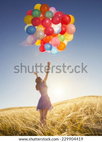 Girl with balloons in nature. Happy woman in a field at sunset. Holidays.