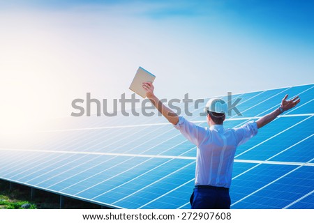 Happy working solar station raising his hands with tablet computer on a background of photovoltaic panels. Science solar energy.