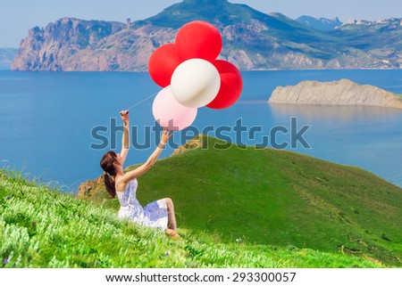 Woman with balloons sitting on the grass of a beautiful landscape. Holiday Photo. Birthday. Celebration.