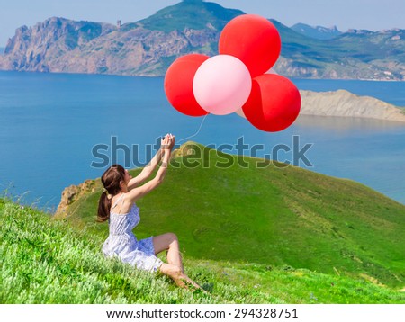 Woman with balloons sitting on the grass of a beautiful landscape. Holiday Photo. Birthday. Celebration.
