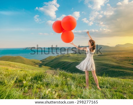 Woman with balloons in field grass on mountains a beautiful landscape outdoors. Girl playing with balloons in the holiday.