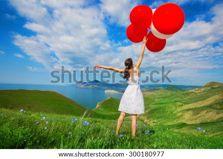 Happy woman with balloons into the field with green grass on the background of beautiful landscape. Celebration on nature outdoors.