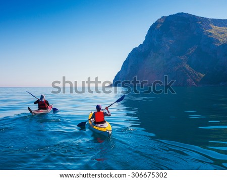 Kayaks. Couple kanoeing in the sea near the island with mountains. People kayaking in the ocean.