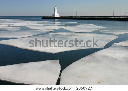 sheets of ice melt in harbour by lighthouse