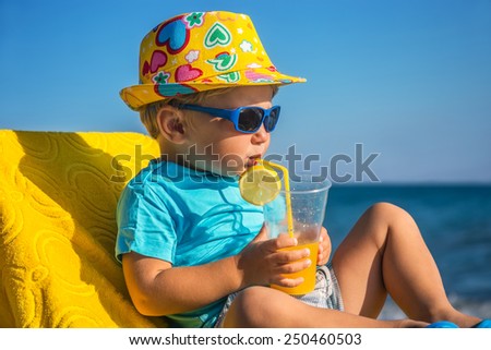 Amusing kid drinks juice from tubule against sea in sunny day