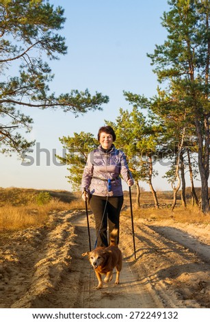 Happy woman with sticks for walking and dog on walk in wood