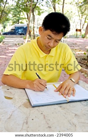 Thai man sitting outside at a table and writing