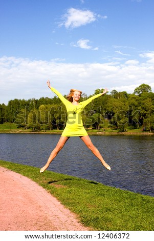 The happy girl jumps on the bank of the summer river