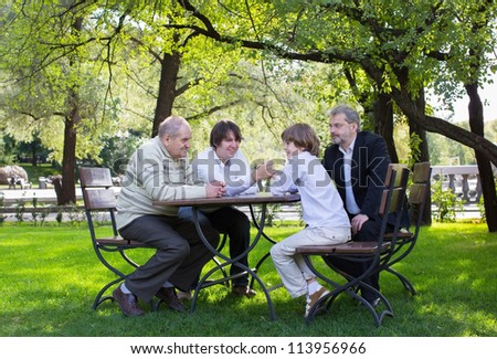 Great-grandfather, grandfather, father and son wrestling at a wooden table in a park