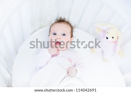 Sweet baby girl in a white round crib with pink bunny toy
