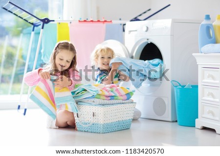Children in laundry room with washing machine or tumble dryer. Kids help with family chores. Modern household devices and washing detergent in white sunny home. Clean washed clothes on drying rack.  Foto stock © 